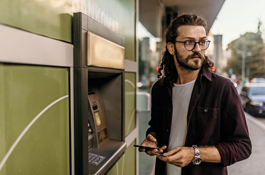 Na obrázku stojí muž u bankomatu a ohlíží se