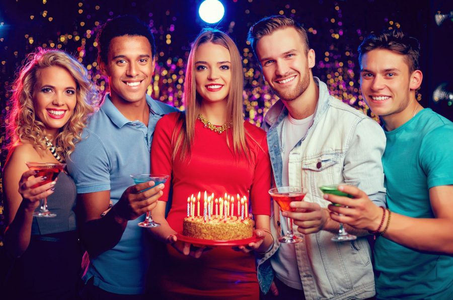 Na obrázku je pět lidí koukajících do kamery, čtyři z nich drží sklenku s přípitkem a žena uprostřed drží dort se svíčkami