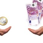 Na obrázku jsou proti sobě dvě ruce, nad jednou se vznáší mince 1€ a nad druhou několik 500€ bankovek