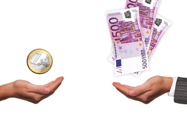 Na obrázku jsou proti sobě dvě ruce, nad jednou se vznáší mince 1€ a nad druhou několik 500€ bankovek