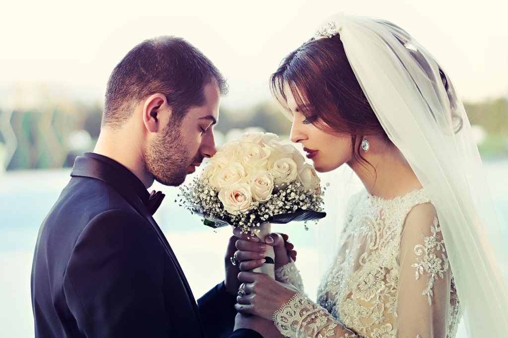 Na obrázku jsou novomanželé společně čichající ke svatební kytici