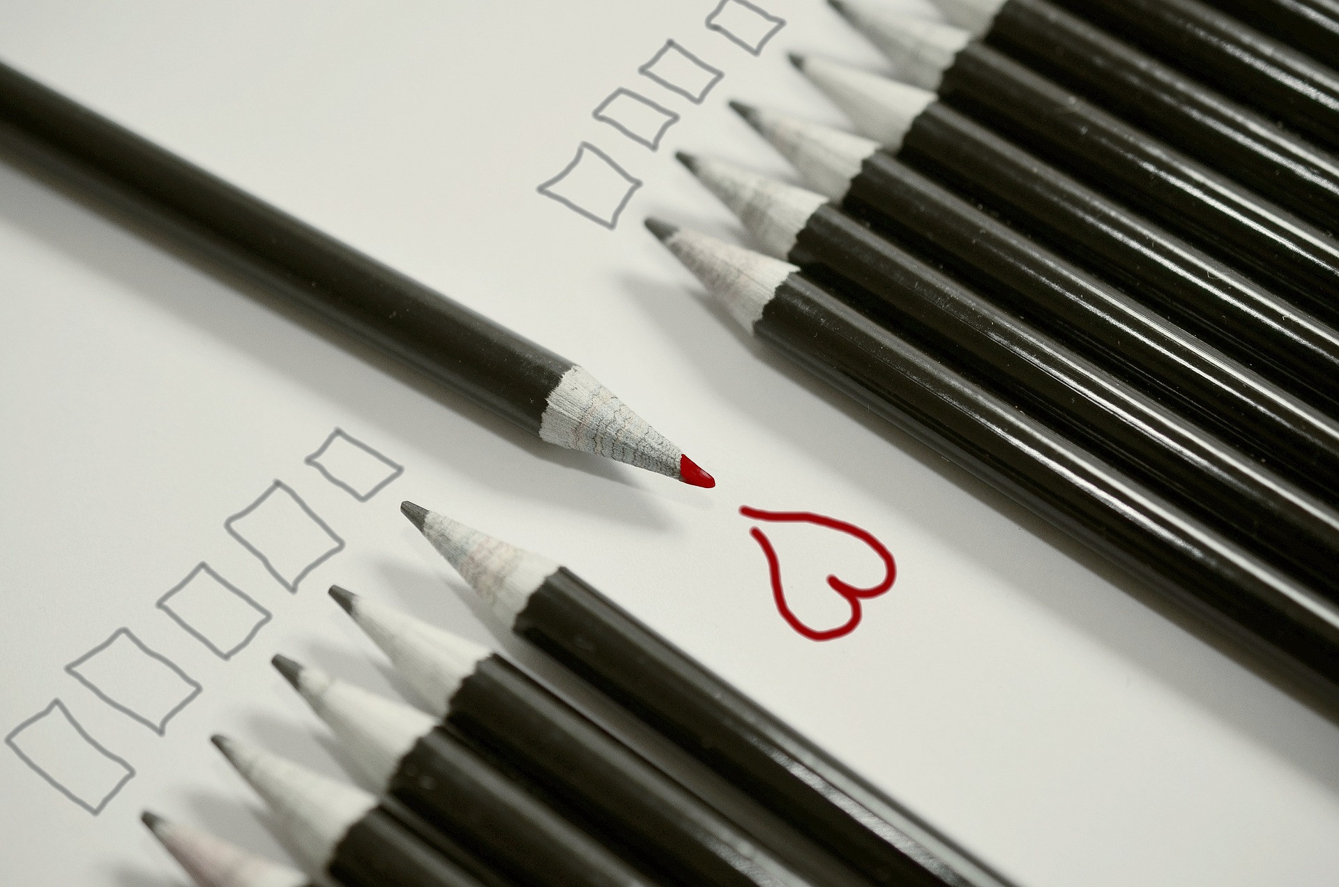 Na obrázku jsou černé tužky kreslící kostičky a jedna červená, která nakreslila srdce