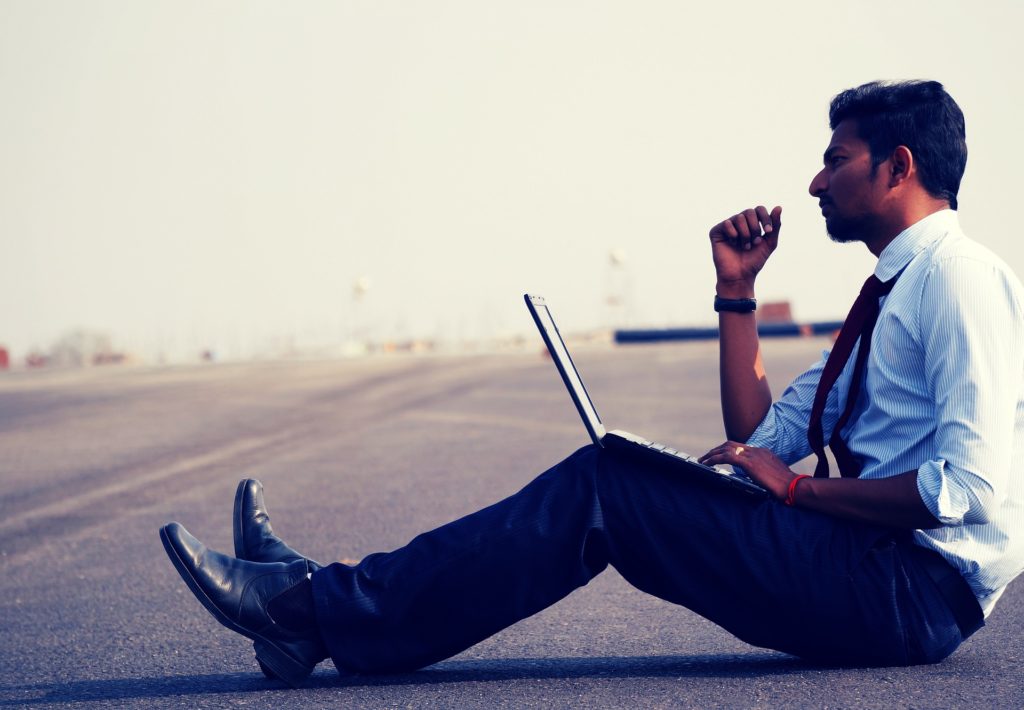 Na obrázku sedí muž uprostřed silnice a pracuje na notebooku