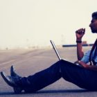 Na obrázku sedí muž uprostřed silnice a pracuje na notebooku