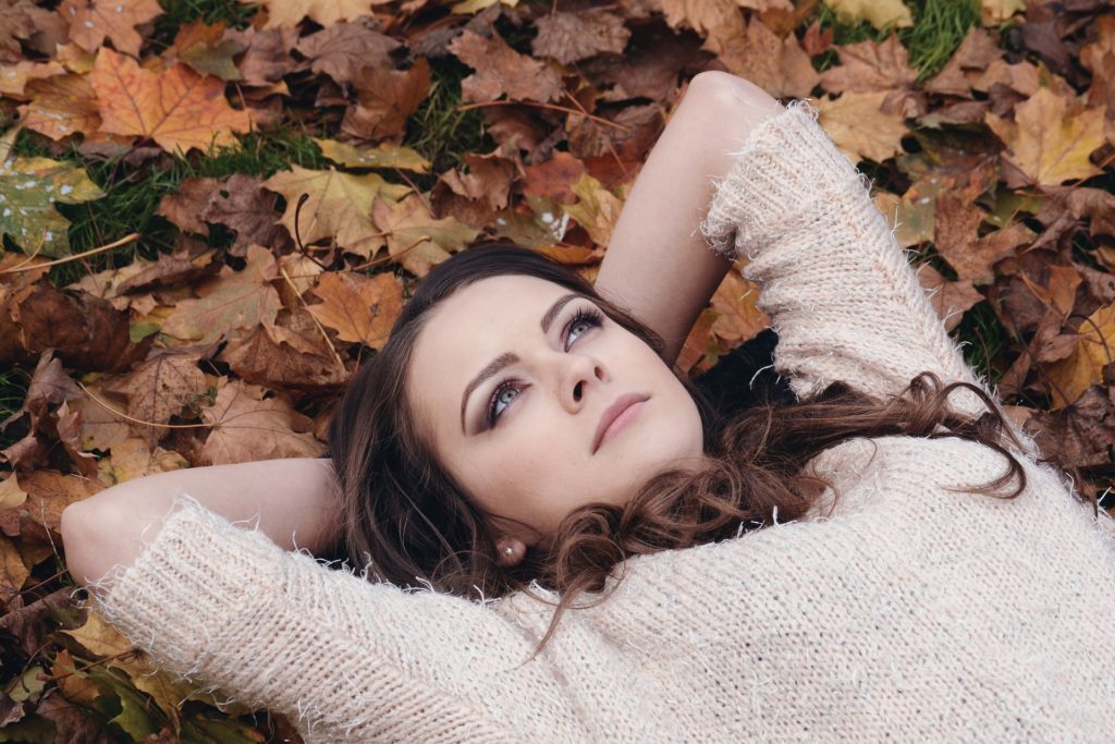 Na obrázku je žena ležící v listí s rukama složenýma za hlavou, jak zamyšleně kouká vzhůru