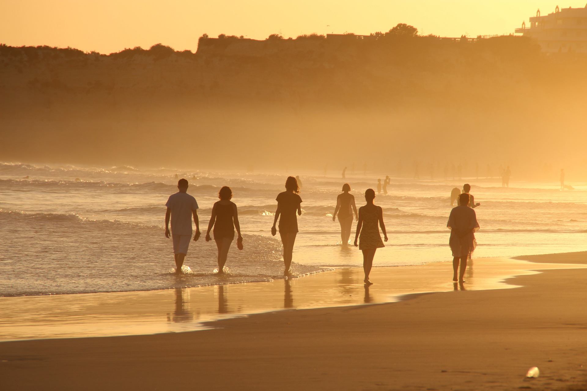 Na obrázku jsou lidé jdoucí po pláži při západu slunce