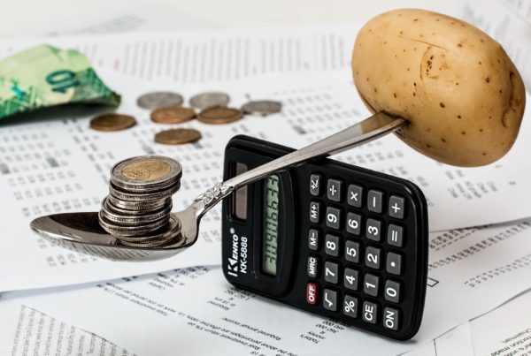 Na obrázku je na boku postavené kalkulačka, na které balance lžíce - ta má na jedné straně sloupeček mincí a na druhé syrový brambor.