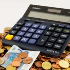 Na obrázku je kalkulačka položená na kupce mincí a bankovek