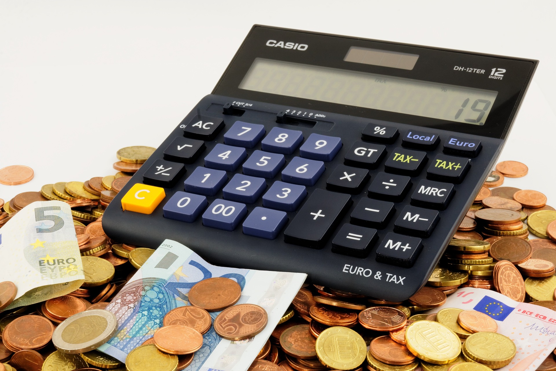 Na obrázku je kalkulačka položená na kupce mincí a bankovek