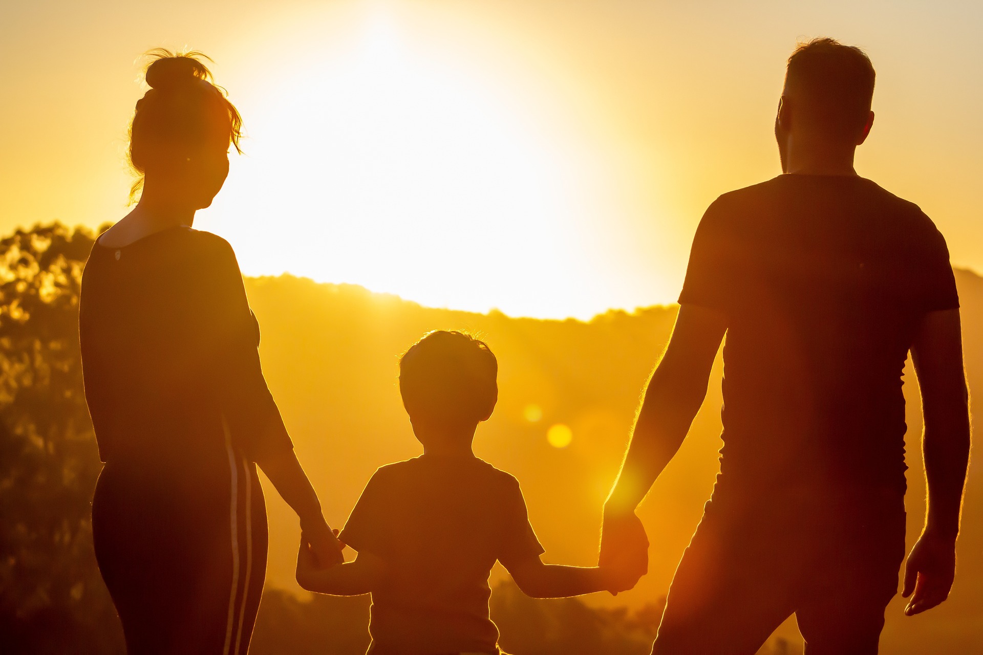 Na obrázku je muž a žena držící mezi sebou dítě při západu slunce