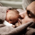 Na obrázku je novorozenec spící na hrudníku otce