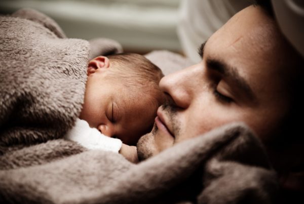 Na obrázku je novorozenec spící na hrudníku otce