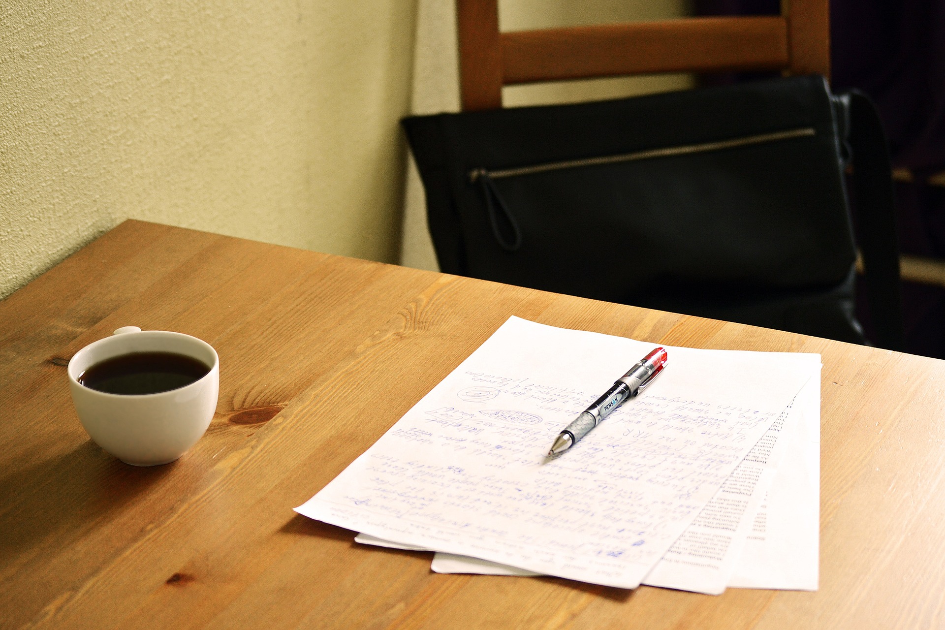 Na obrázku jsou na stole položené papíry a na nich pero, vedle stojí šálek s kávou