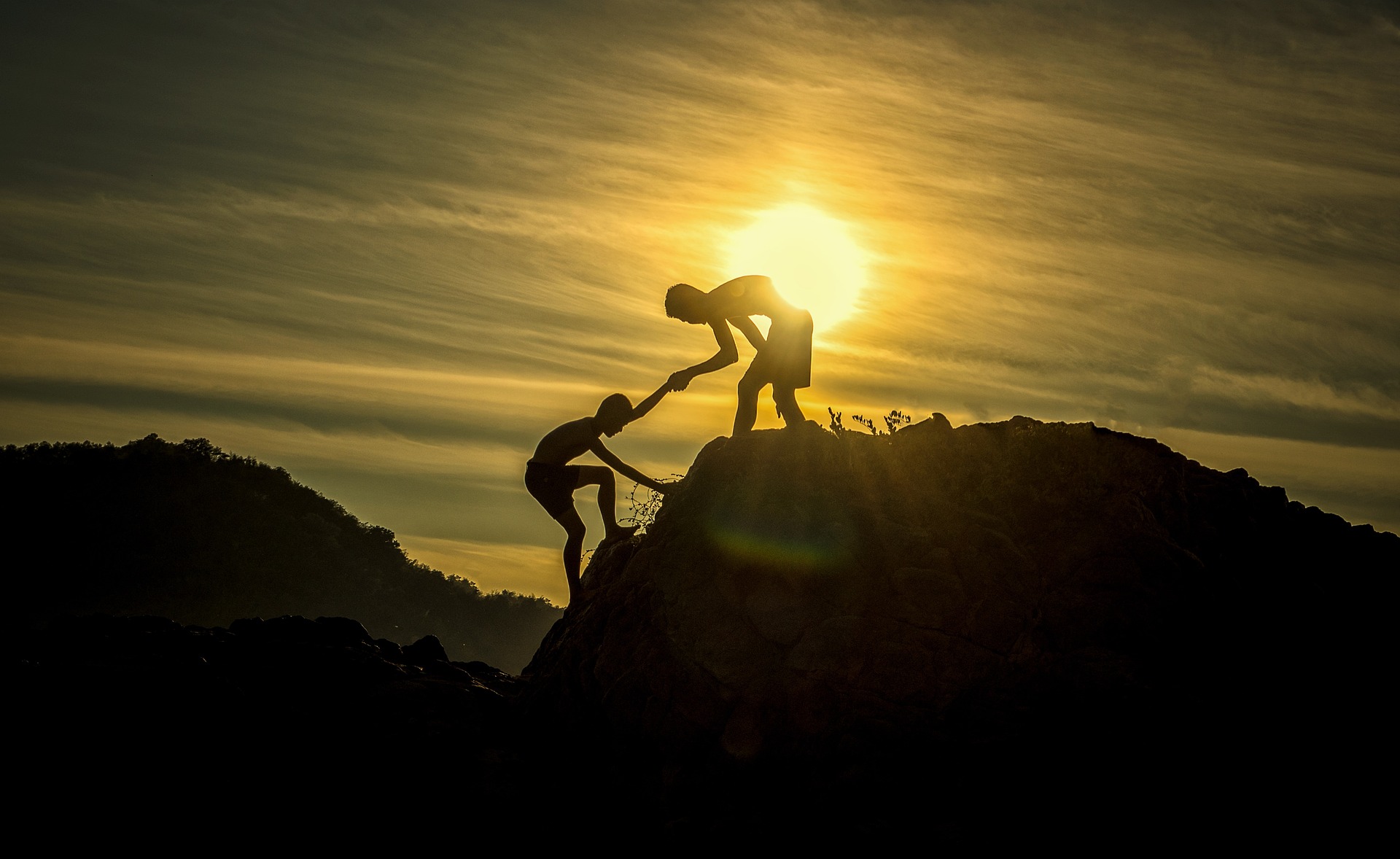 Na obrázku pomáhá jedna osoba druhé vylézt na vrchol kopce.