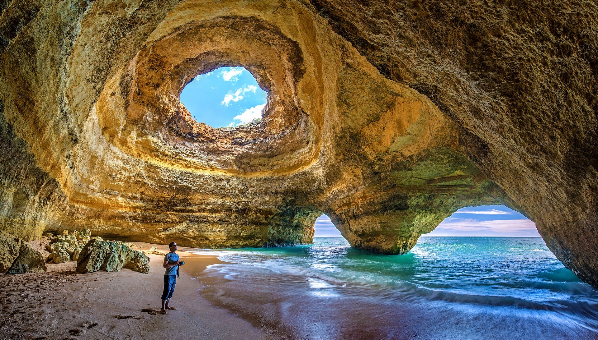 Na obrázku je člověk stojíci v jeskyni u moře