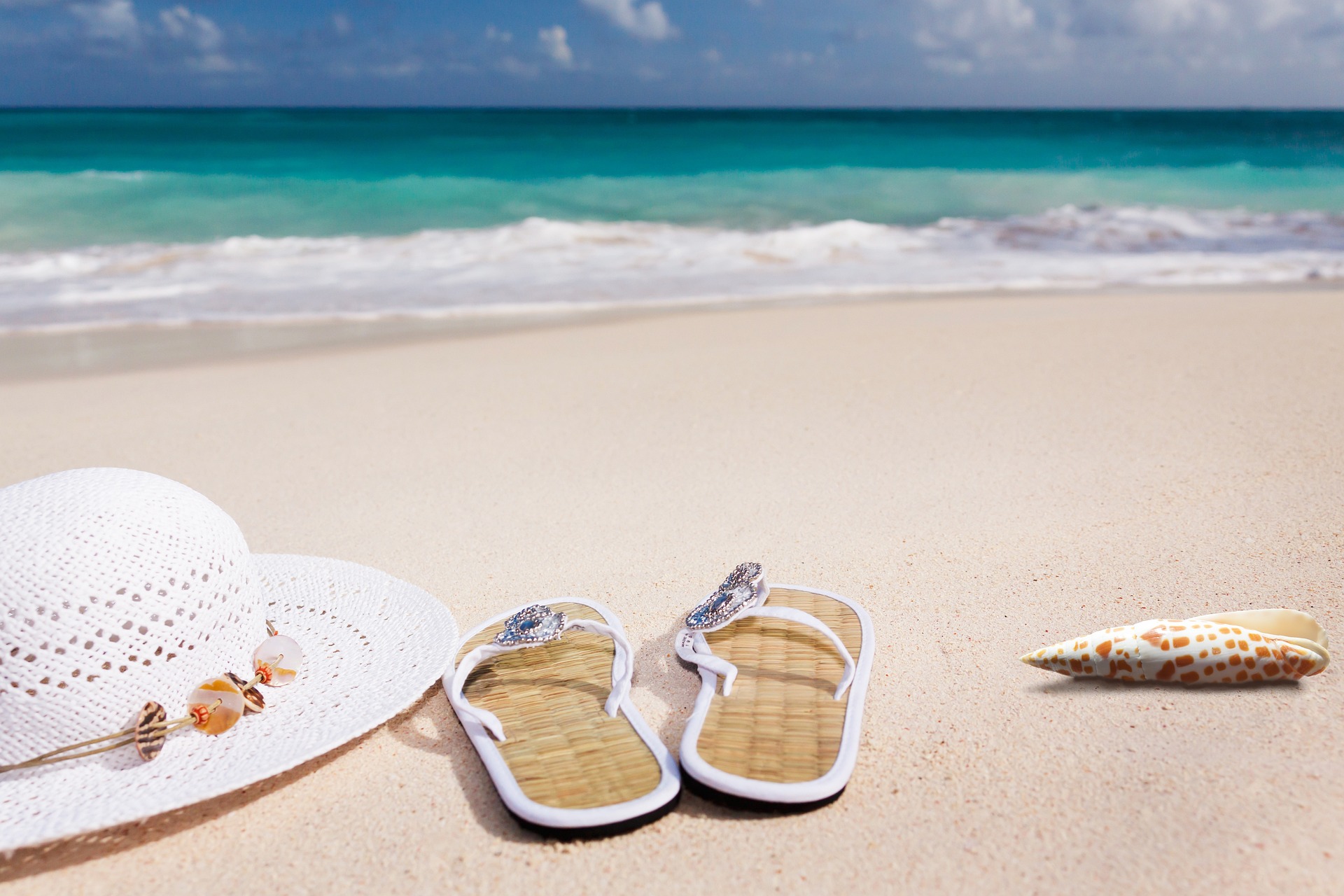 Na obrázku je klobouk a sandále položené na pláži u moře