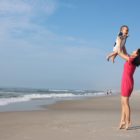 Na obrázku zvedá žena na pláži do vzduchu kojence