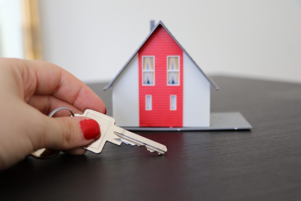 Na obrázku je miniatura domu a ruka držící klíč