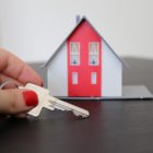 Na obrázku je miniatura domu a ruka držící klíč