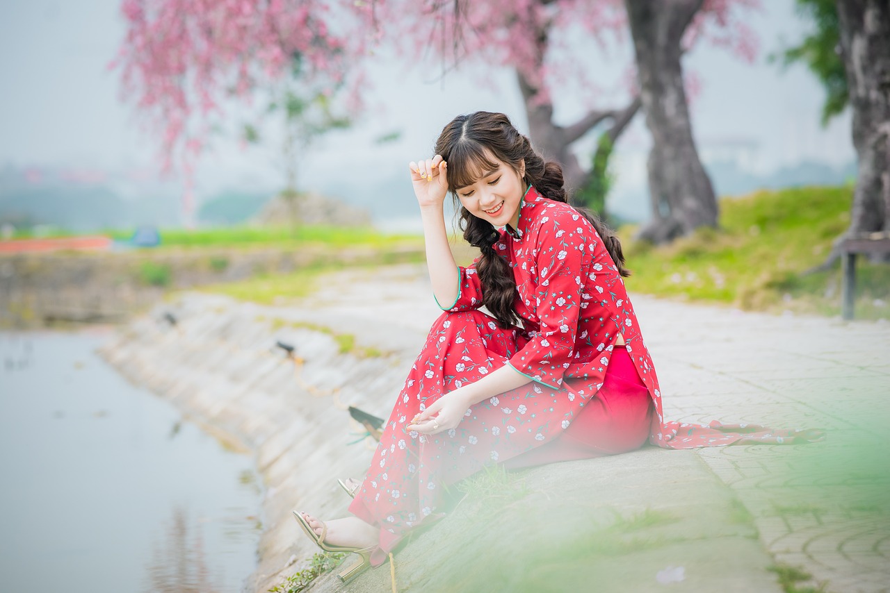 Na obrázku je žena asijského původu sedící u vody v třešnové zahradě